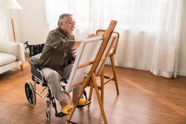 Old senior asian male using art therapy while his legs is injured at homeasian elder man spend recovering of his leg is getting better with painting canvas art in living room at home