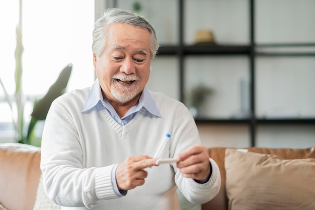 Old senior retired asian male hand hold gesture and show covid19 rapid test kit result with negative sign with happiness and cheerfulself test rapid test at home