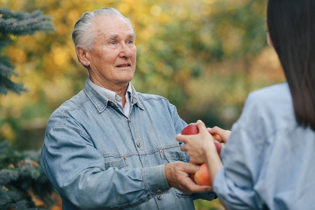 Old senior standing in a summer garden with apples