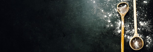 Old spoons on dark table with flour