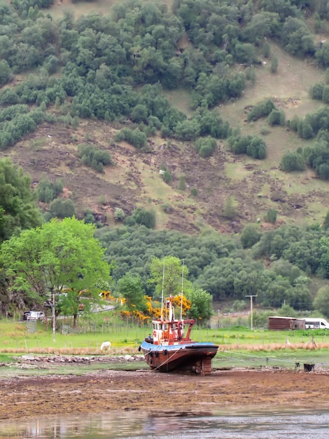 An old tugboat stranded on the shore of a lake in Scotland United Kingdom