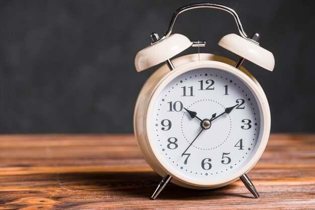 An old vintage alarm clock on wooden desk against black background