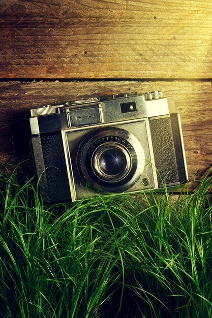 Old Vintage Camera in Green Grass with Light Beams on Wooden Background. Top View.