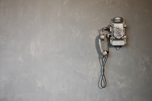 Старый винтажный проводной телефон для связи висит на текстурированной серой стене. старинный телефон из прошлого для фона. история телефона в мире. понятие связи и телеграфа. копировать пространство