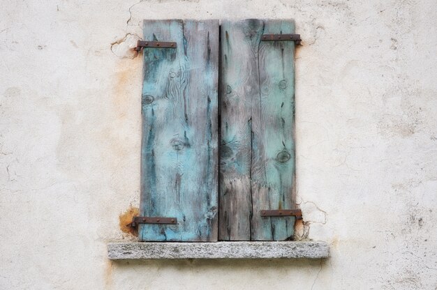 青いさびた木製シャッター付きの古い風化した壁