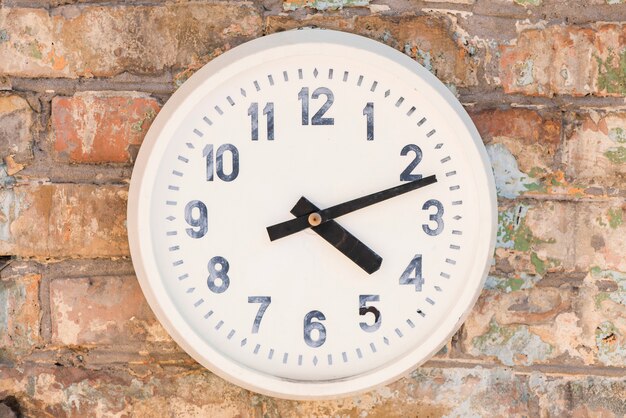 An old white clock against weathered brick wall