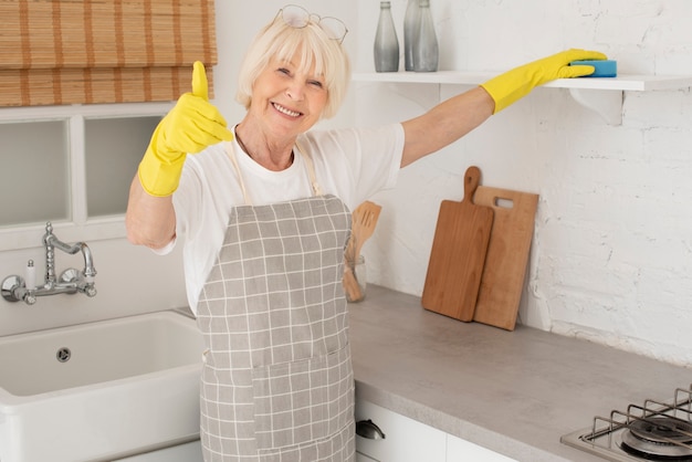 Old woman cleaning the kitchen with gloves