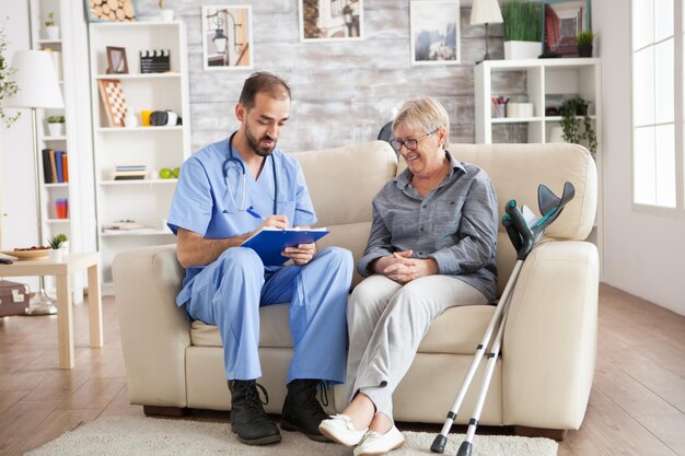 Old woman in nursing home laughing while doctor taking notes on clipboard.