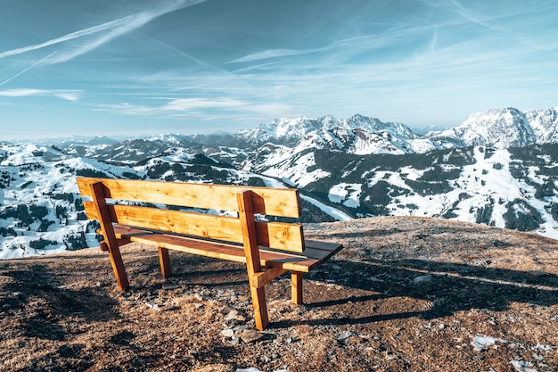Старая деревянная скамейка на вершине скалы с красивыми скалистыми горами, покрытыми снегом в