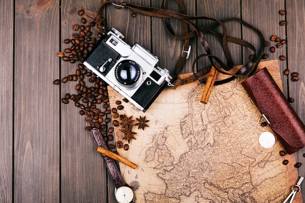 Old yellow map, glasses, coins, leather case, camera, watch, compasses, coffee beans, other spices and cookies lie on wooden floor