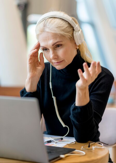 Older business woman having a video call on laptop with headphones