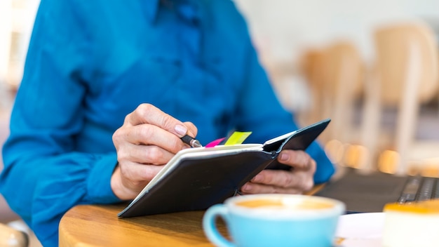 Older business woman working on laptop and writing in agenda