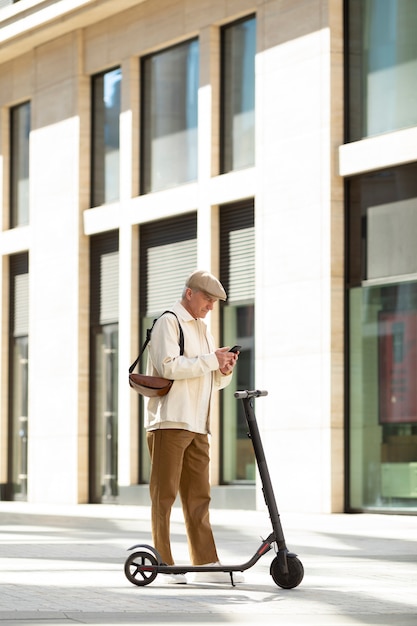 Free photo older man in the city with an electric scooter using smartphone