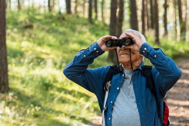 쌍안경으로 야외에서 자연을 즐기는 노인