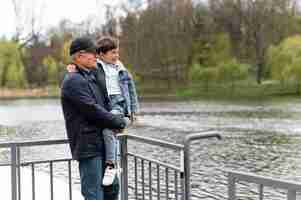 Free photo older man holding his grandson in the park near the lake