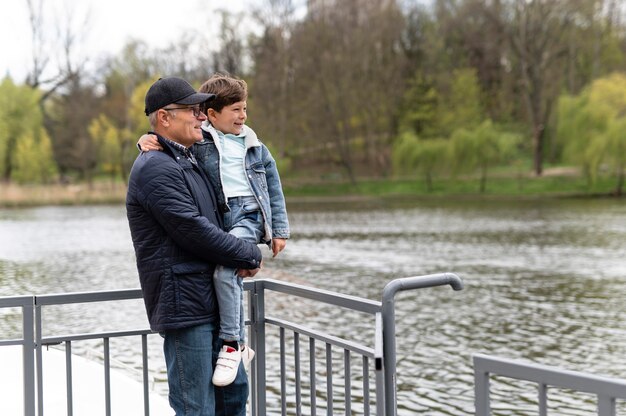湖の近くの公園で孫を抱いている年配の男性