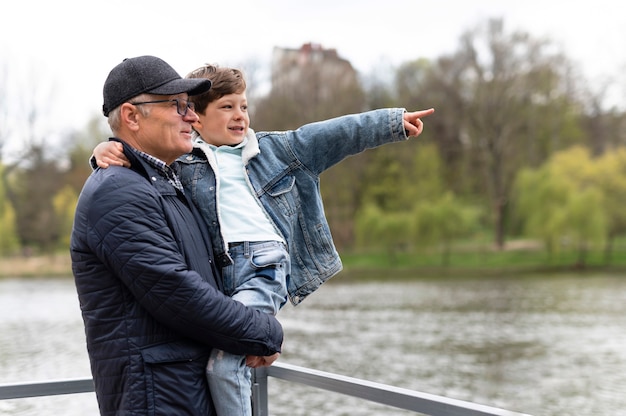 Пожилой мужчина держит внука в парке у озера