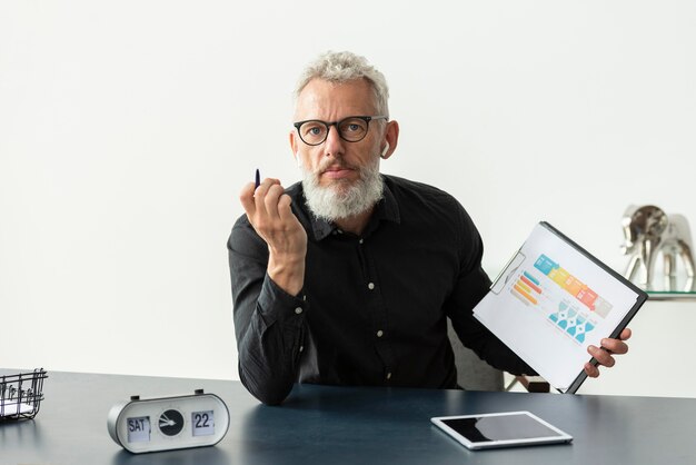 Older man at home showing graph on notepad with tablet on desk