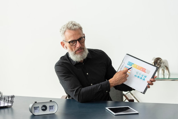 Free photo older man at home showing graph on notepad with tablet on desk