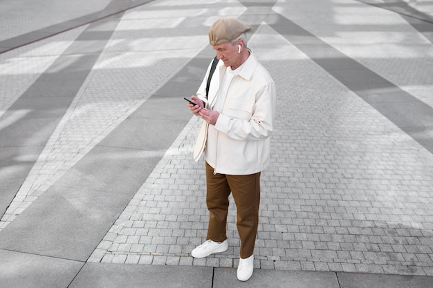 イヤフォン付きのスマートフォンを使用して街の屋外で年配の男性