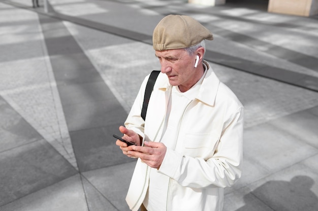 Older man outdoors in the city using smartphone with earbuds