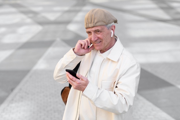 Uomo anziano all'aperto in città utilizzando smartphone con auricolari