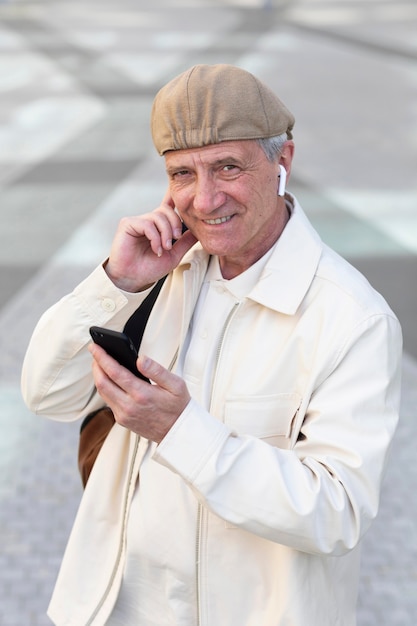 Older man outdoors in the city using smartphone with earbuds