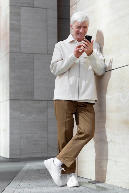 Older man outdoors in the city using smartphone with earbuds