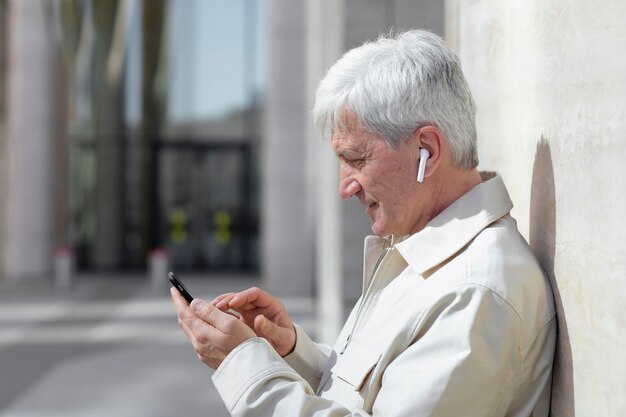 Older man outdoors in the city using smartphone with earbuds