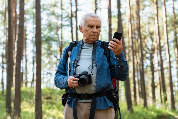Пожилой мужчина с камерой и смартфоном, изучает природу
