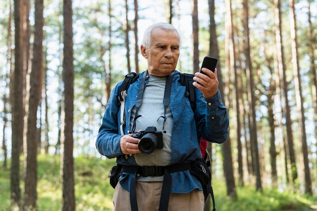 Older man with camera and smartphone exploring nature