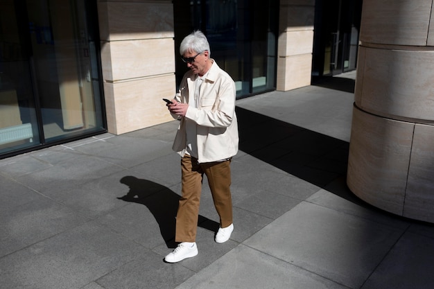 Older man with sunglasses outdoors in the city using smartphone while having coffee