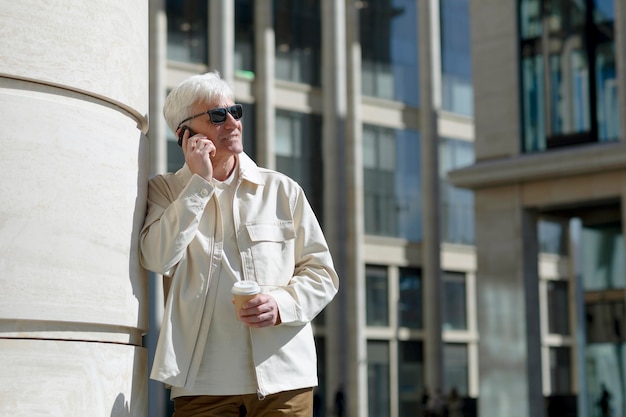 Пожилой мужчина в темных очках на открытом воздухе в городе разговаривает по телефону