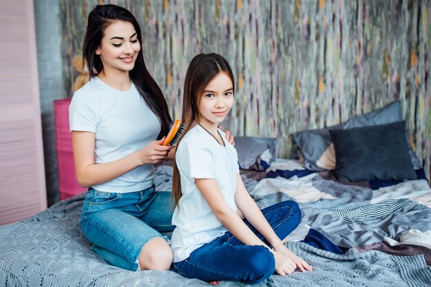 Older sister preparing little to school and combing her hair in bedroom with hairbrush