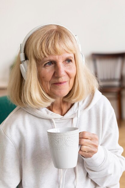 Older woman having coffee and listening to music on headphones