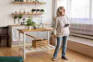 Free photo older woman at home listening to music on headphones and using smartphone