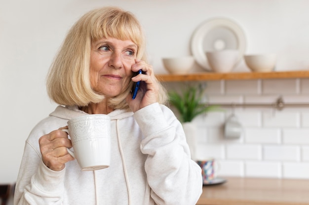 Foto gratuita donna anziana a casa a parlare al telefono mentre beve il caffè