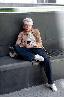 ベンチ​に​座って​スマート​フォン​を​使用して​街​の​屋外​で​年上​の​女性