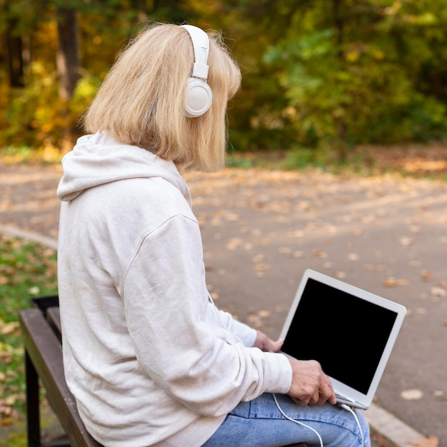 Older woman outdoors with laptop and headphones