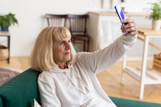 Foto gratuita donna anziana che prende un selfie a casa