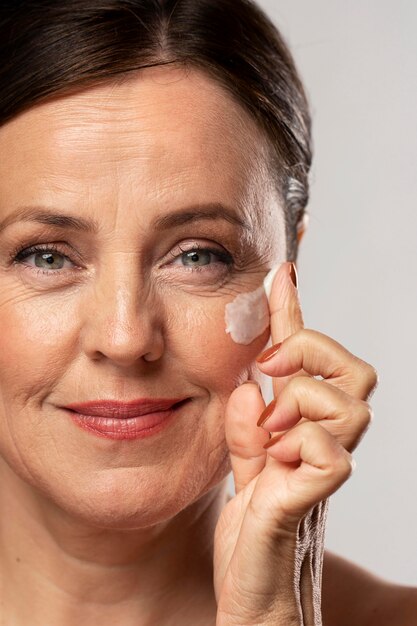 Пожилая женщина использует увлажняющий крем на лице