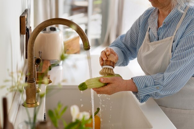 Foto gratuita donna più anziana che lava le verdure in cucina