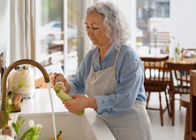 Пожилая женщина моет овощи на кухне
