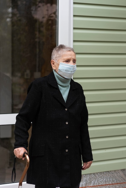 Пожилая женщина в медицинской маске с тростью