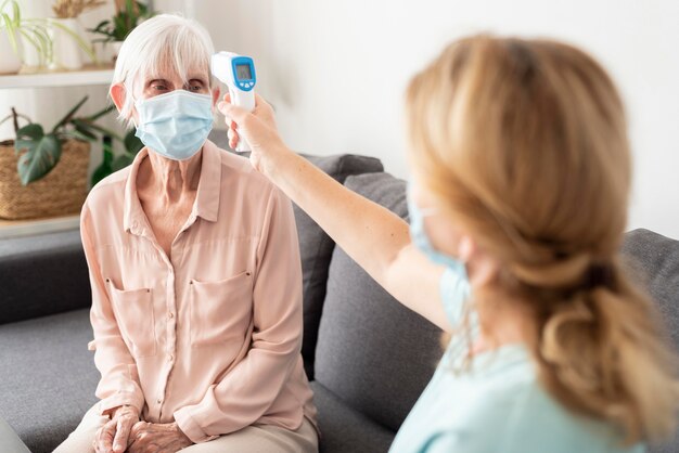 Пожилая женщина в медицинской маске проверяет температуру у медсестры