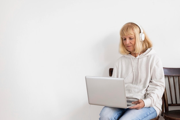 Free photo older woman working on laptop at home and wearing headphones