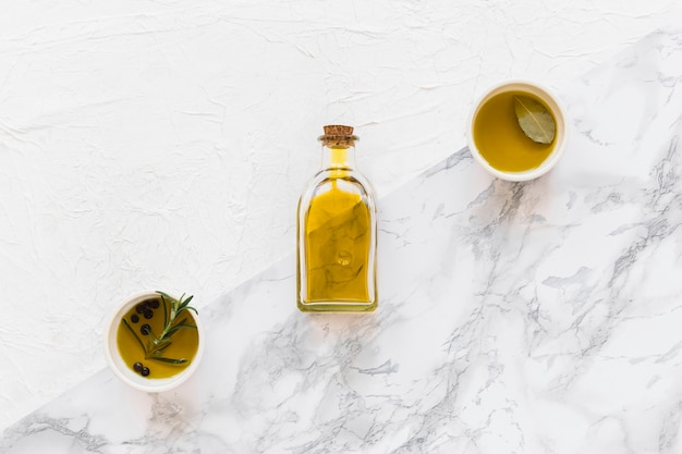 Free photo olive and black pepper oil in bowl and bottle on two textured backdrop