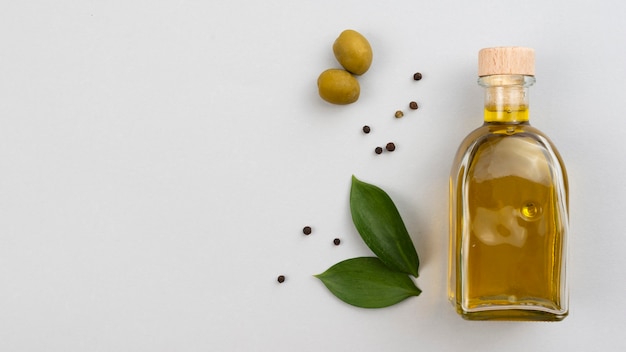 Бутылка оливкового масла с листьями и оливками на столе