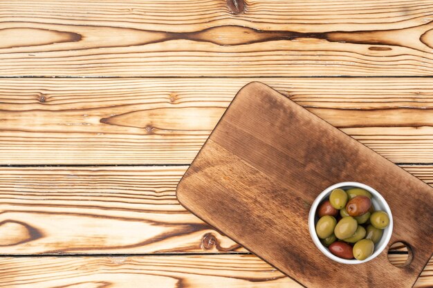 Оливки в миске на деревянном фоне вид сверху