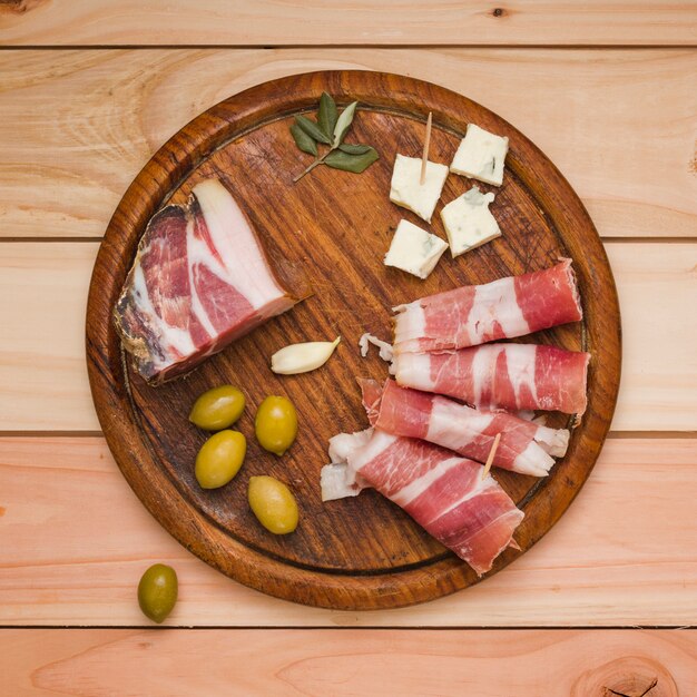Olives; garlic clove; cheese slice and bacon on wooden tray over the desk